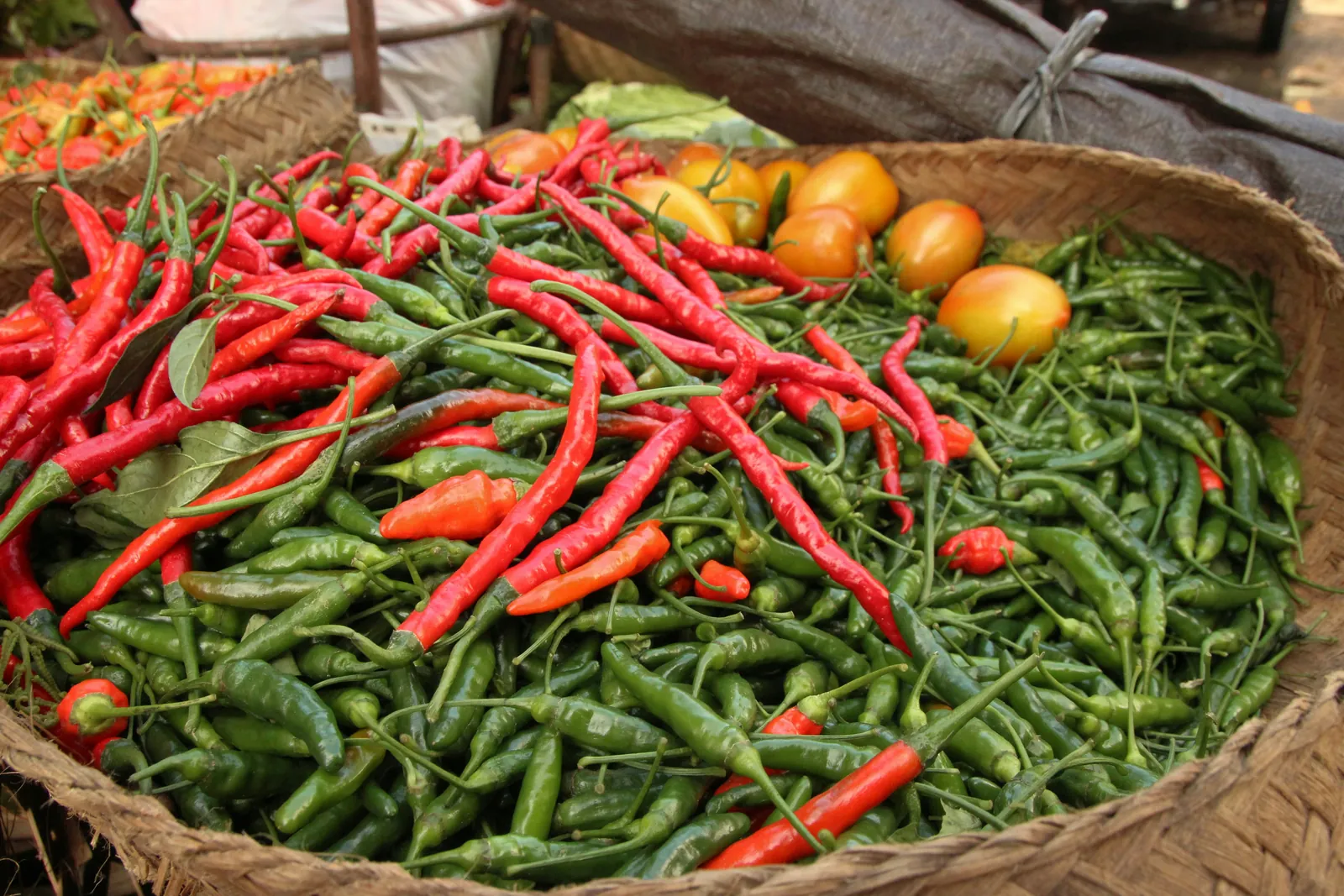 Woven basket piled with red and green chillies and a few tomatoes on a Bali market stall