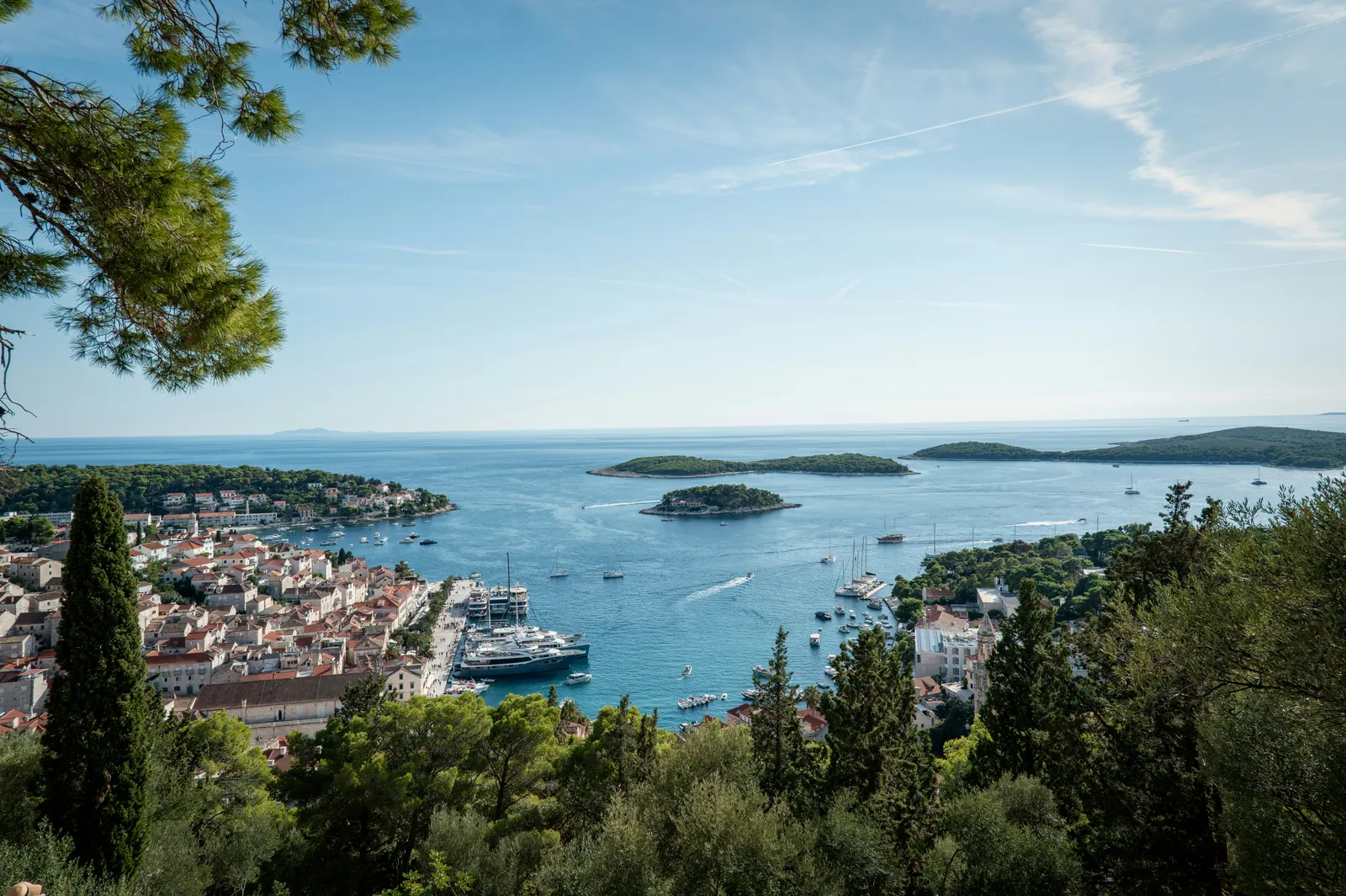View from a pine-covered hill over the red roofs of Hvar town and its harbour full of yachts, to small wooded islands in a calm blue sea
