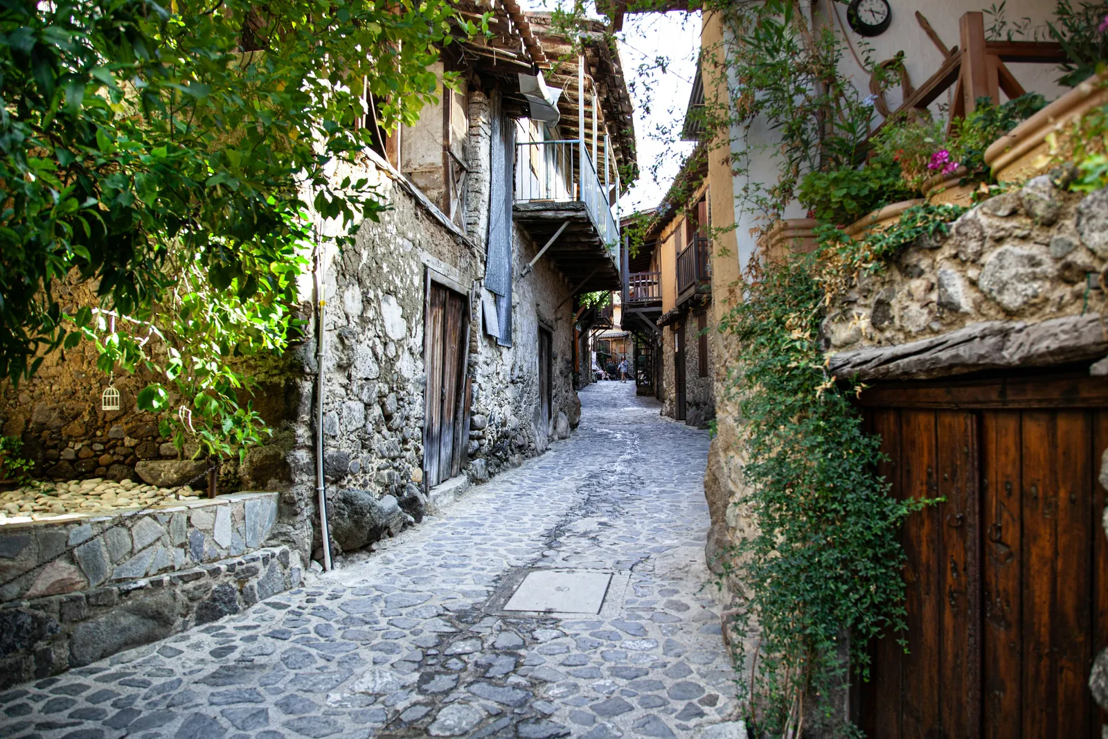 A narrow cobbled lane between old stone houses with wooden balconies, climbing plants and weathered doors in Kakopetria