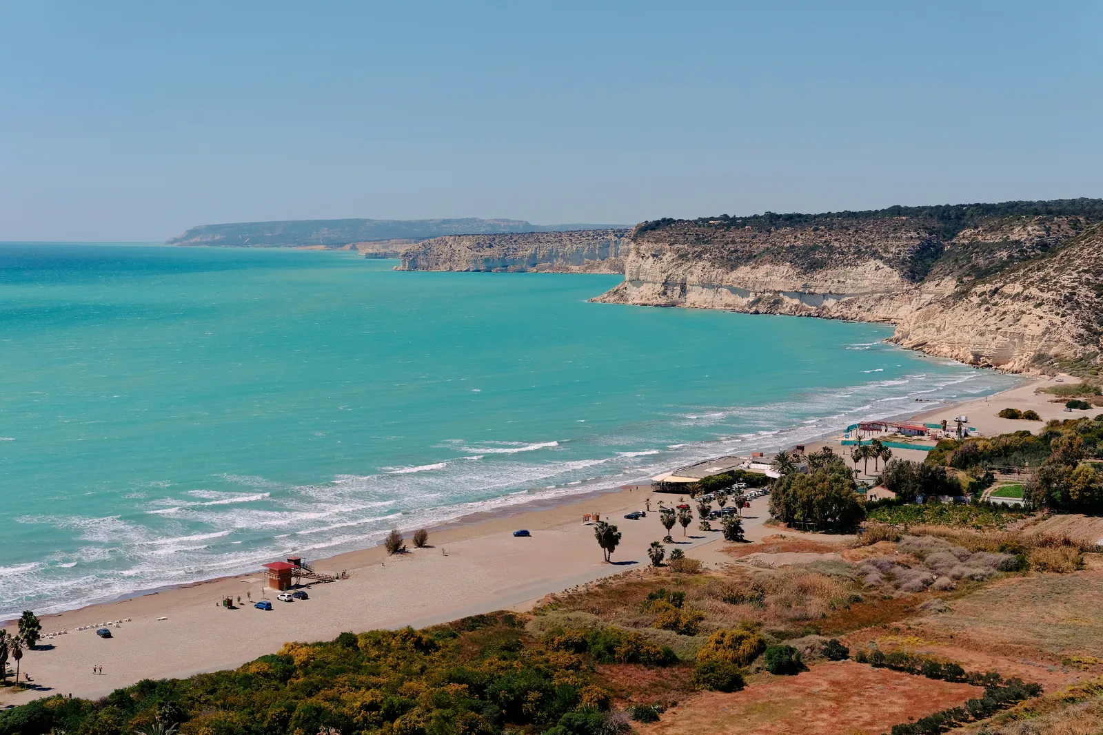 A long sandy beach curving under pale cliffs, with turquoise sea and white surf, west of Limassol