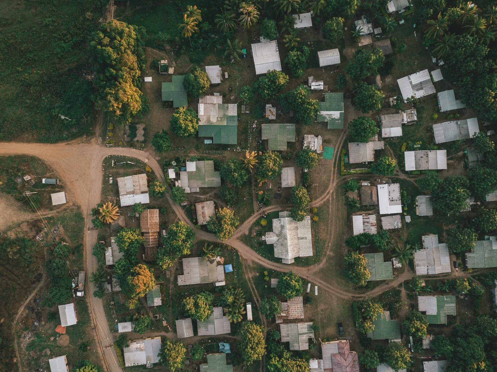 A Fijian village seen from directly above, with iron-roofed houses among shady trees and red dirt tracks winding between them