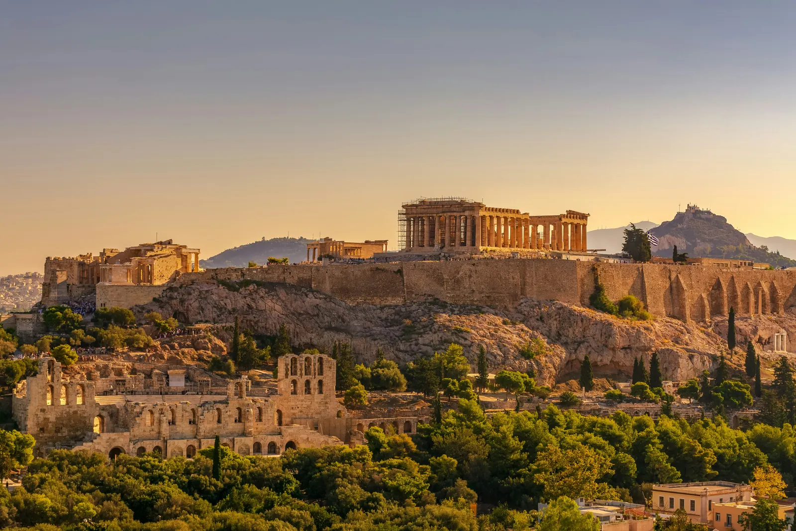 The Parthenon and the walls of the Acropolis in golden evening light above the Odeon of Herodes Atticus, with Lycabettus hill behind