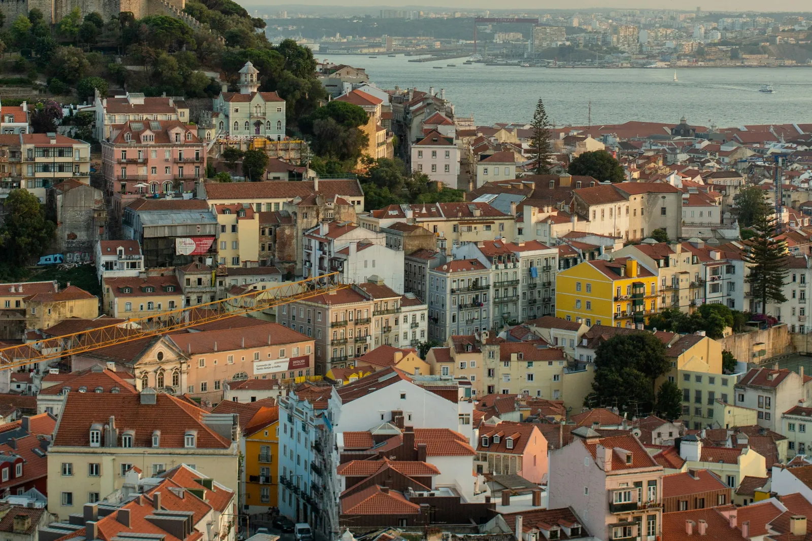A hillside packed with pastel houses and red roofs running down to the wide river, with the far bank in a haze